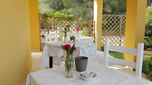 An outdoor patio with a table set for two, a vase with red flowers, and a basket of snacks. - Meravisola (Castiadas)