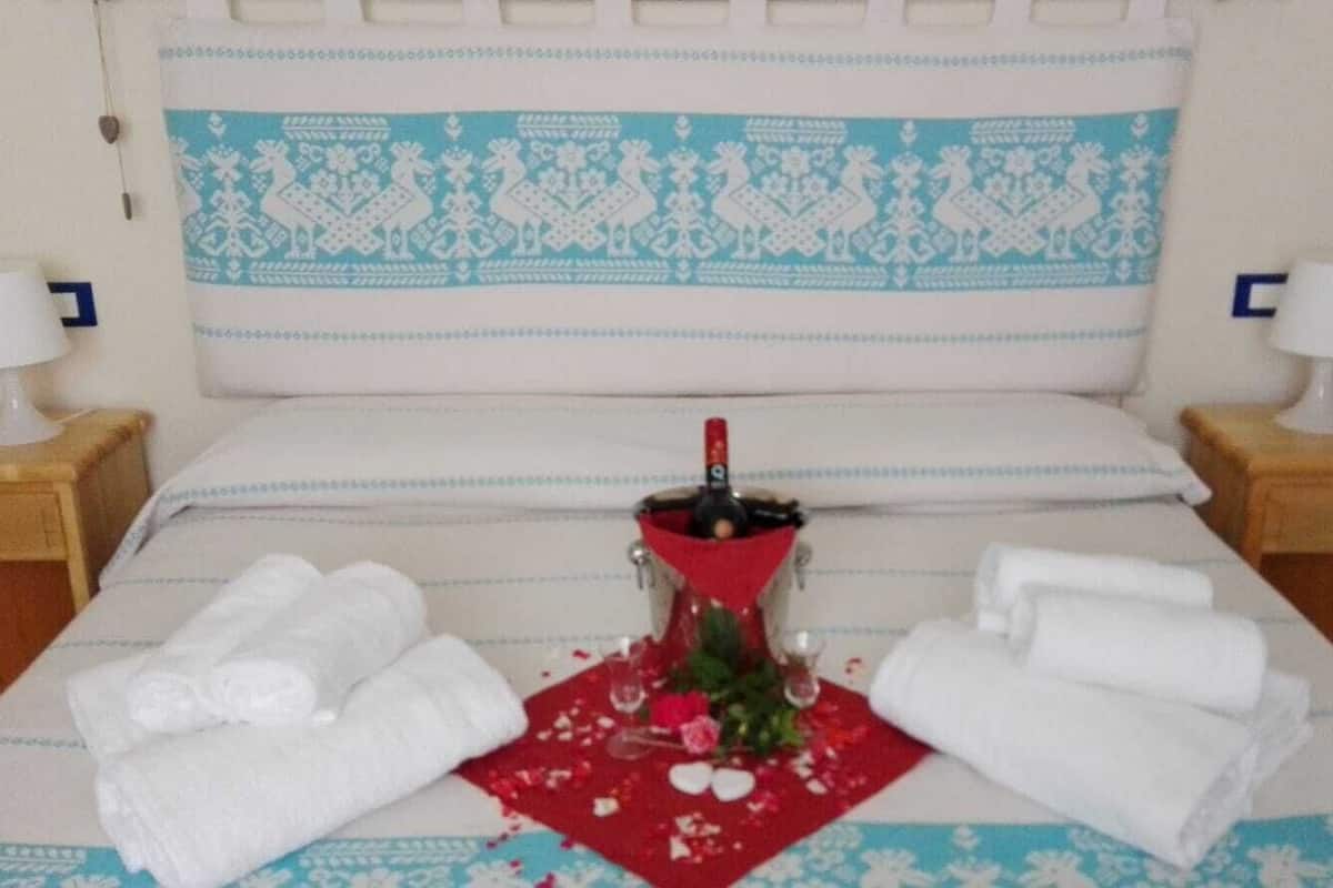 A neatly made bed with a decorative headboard, two bedside tables with lamps, and a bottle of champagne on a red napkin.