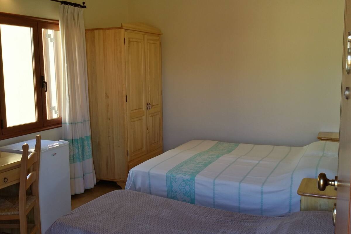 A bedroom with two beds, a desk, a wardrobe, and a window with curtains.