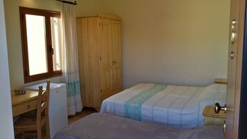 A bedroom with two beds, a desk, a wardrobe, and a window with curtains.