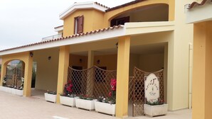 A yellow building with a covered entrance, potted plants, and a sign reading "merVisola Ristorante." - Meravisola (Castiadas)