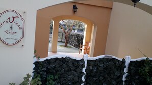 A guest house entrance with a sign reading "merajisola Tostarei guest house," an archway, a small seating area with chairs, and a white fence with a sign that says "ENTRATA." - Meravisola (Castiadas)