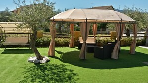 A covered outdoor seating area with a canopy, artificial grass, and a tree. - Meravisola (Castiadas)