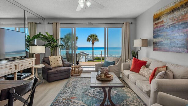 A modern living room with a large TV, comfortable seating, a coffee table, and a view of the beach. - Ocean Front Destin Condo, Newly Redecorated (Destin)
