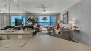 A modern living room with a large TV, a dining area, and a view of the ocean. - Ocean Front Destin Condo, Newly Redecorated (Destin)