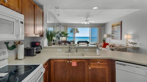 A modern kitchen with a central island, wooden cabinets, and a view of the ocean through large windows. - Ocean Front Destin Condo, Newly Redecorated (Destin)