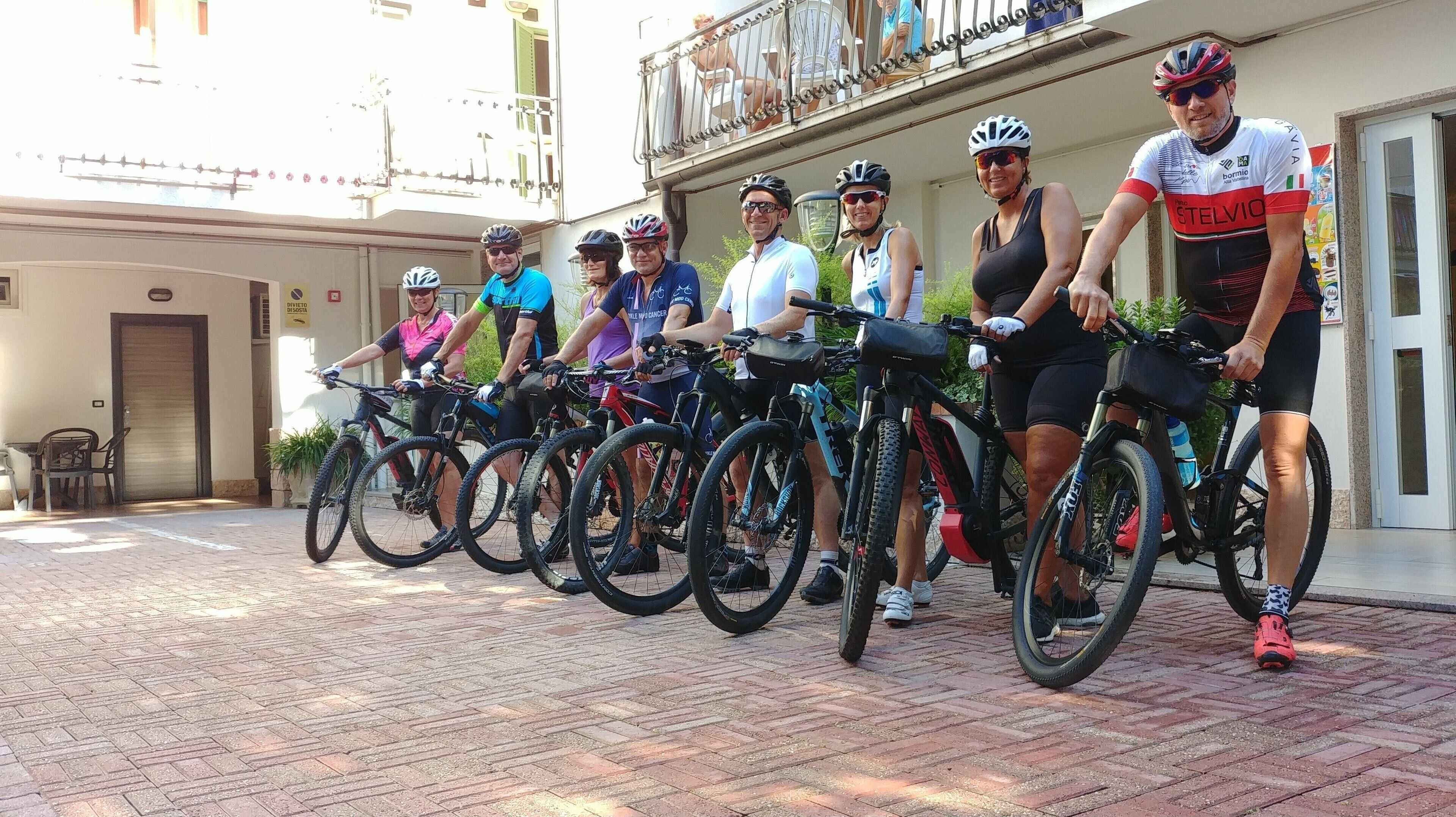 A group of cyclists standing in front of a building with a tiled pavement.