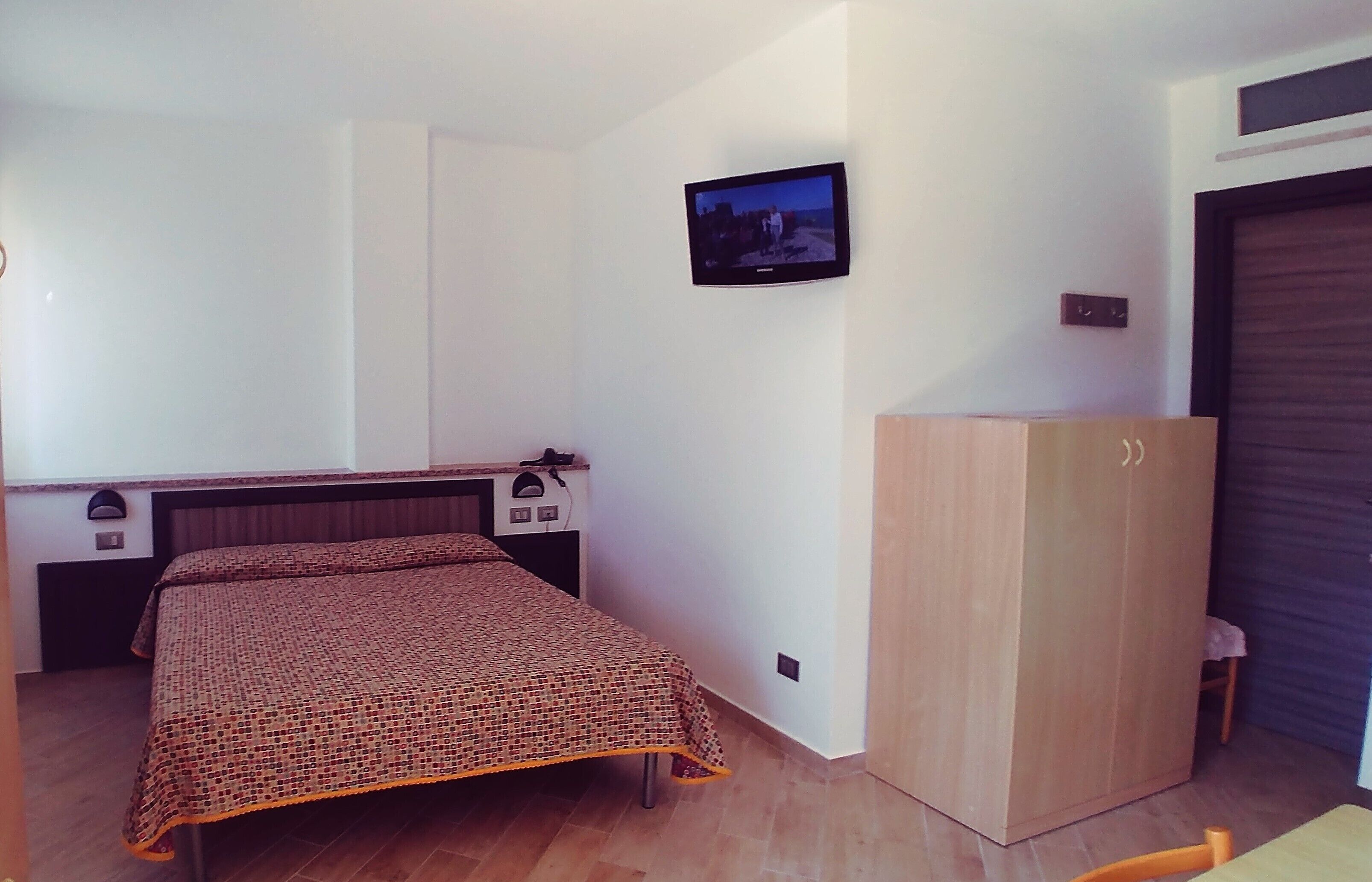 A bedroom with a bed, a wardrobe, a television mounted on the wall, and a small table.