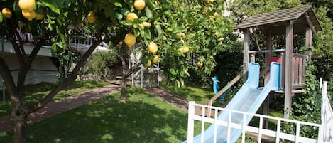 A playground with a blue slide and a tree with yellow fruit.