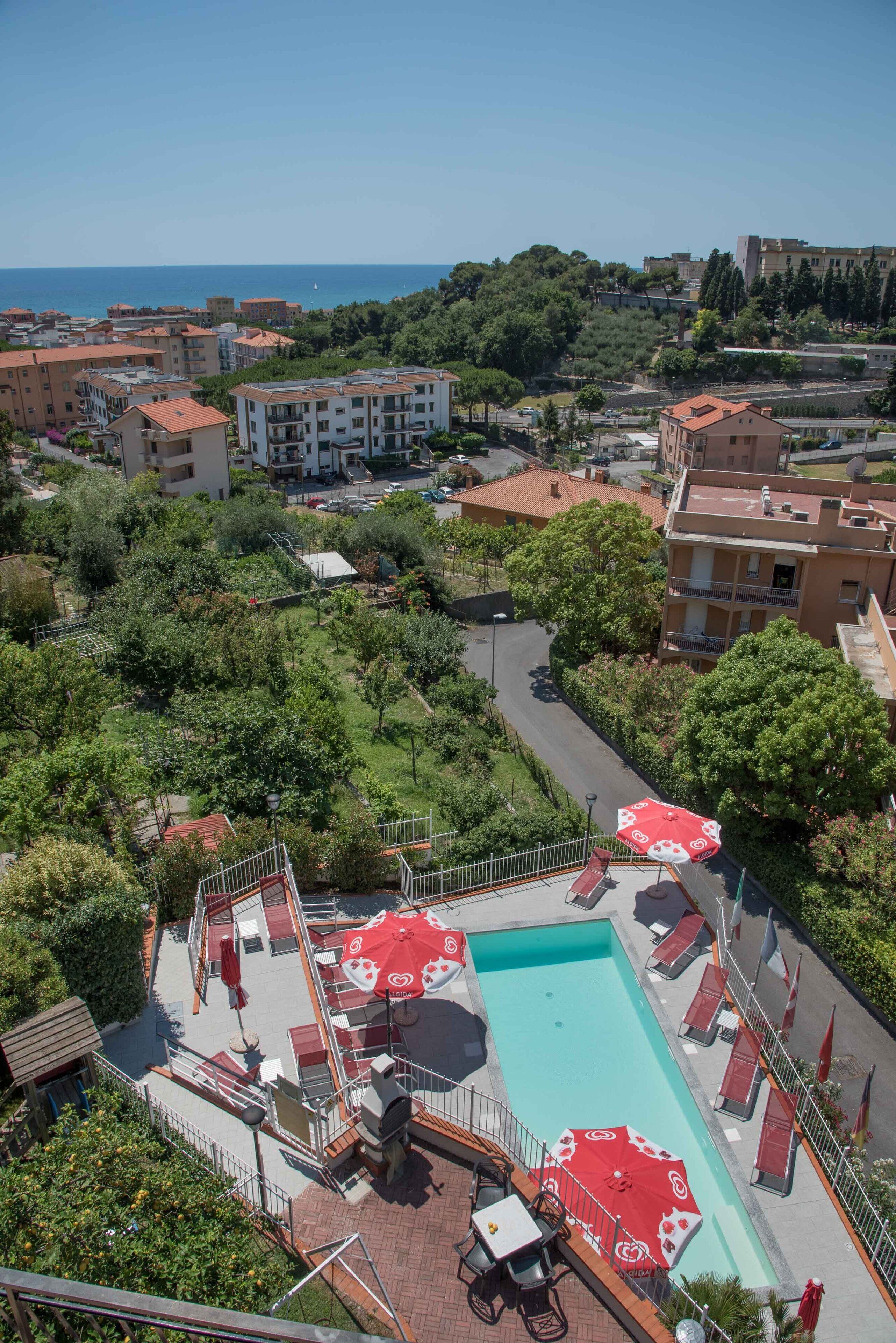 Zona de piscina en la azotea con sombrillas rojas, sillones de descanso y vistas al mar y edificios circundantes.
