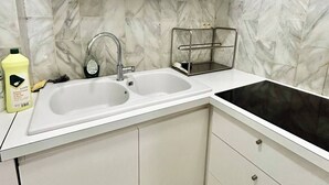 Een keuken met witte kasten, een dubbele spoelbak, een zwart fornuis en een marmeren achterwand.