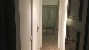 Un passadís estret amb terra de fusta, una taula petita amb un ram i una porta a la dreta.