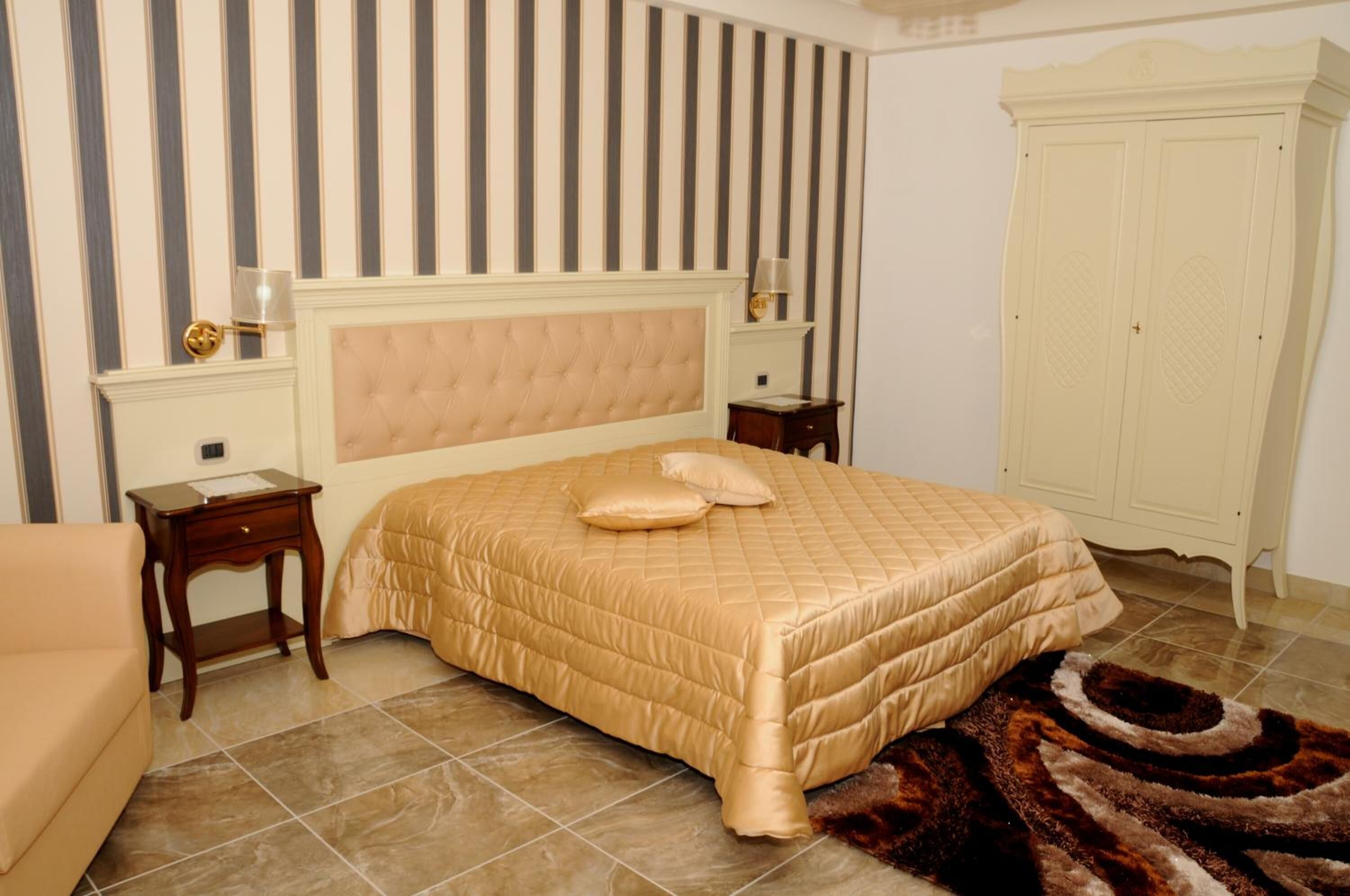 Ein Schlafzimmer mit einem großen Bett, einem Nachttisch, einer Kommode und rautenmusteriger Tapete.