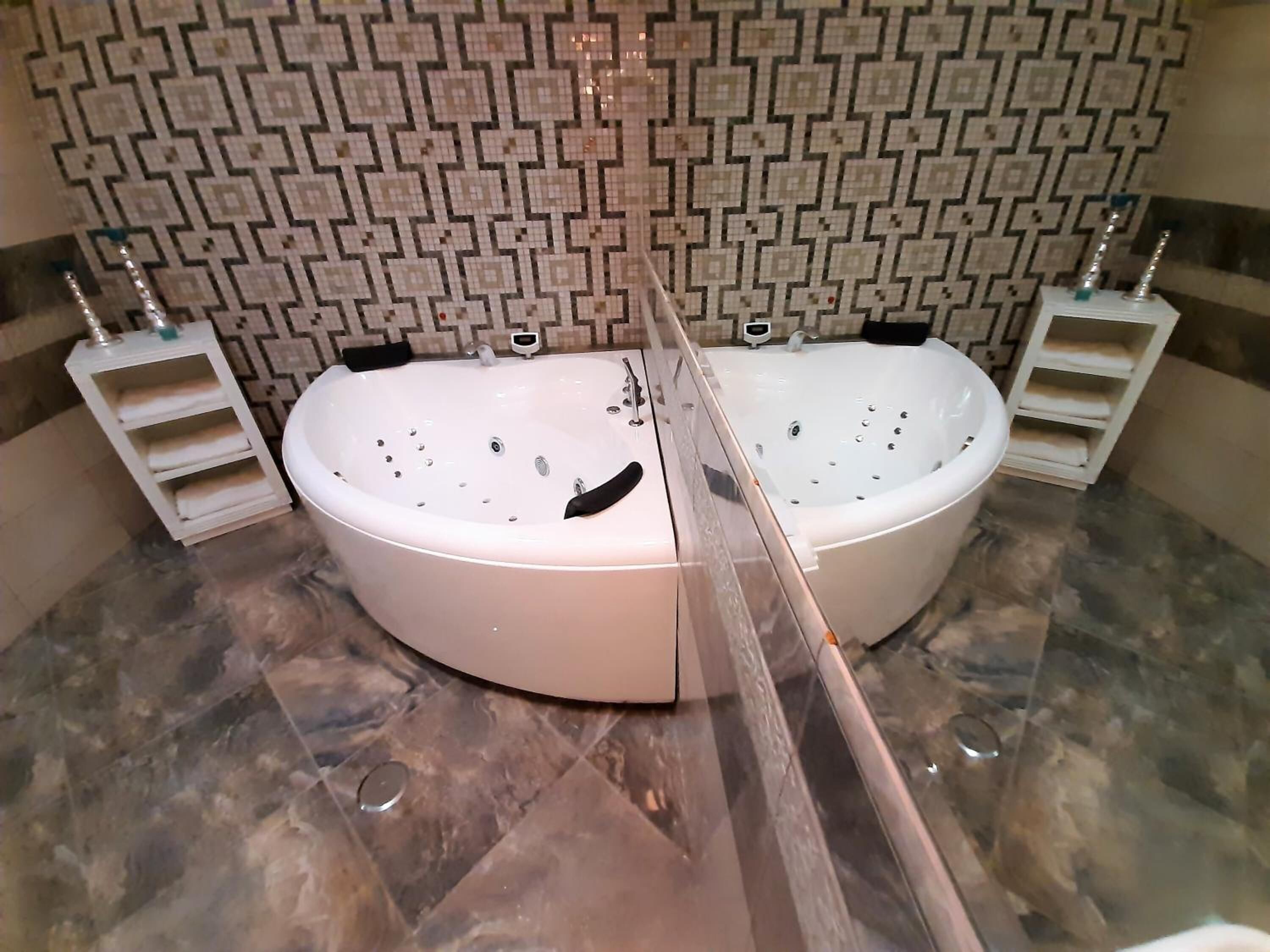A bathroom with two large oval-shaped tubs, a patterned tile backsplash, and a marble floor.