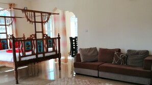 A spacious living area with a high ceiling, a wooden four-poster bed, a striped sofa, and a patterned rug. - Salhiya Lodge - Hostel (Bububu)