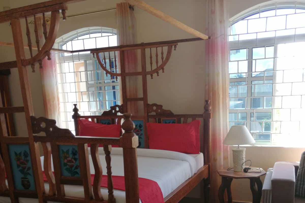 Un lit à baldaquin avec une couvre-lit rouge, une table de chevet en bois, une lampe et un tapis rouge.