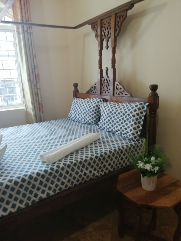 Un lit avec une couvre-lit à motifs, une tête de lit en bois et une table de chevet agrémentée d’une plante.