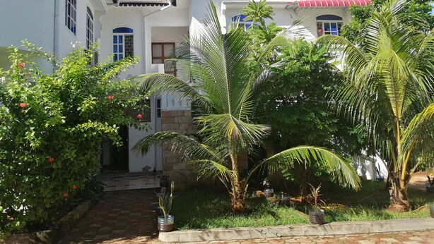 A two-story building with a red roof and white walls, surrounded by lush greenery and palm trees. - Salhiya Lodge - Hostel (Bububu)