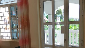 A room with a large sliding glass door leading to an outdoor balcony with a white balustrade. - Salhiya Lodge - Hostel (Bububu)