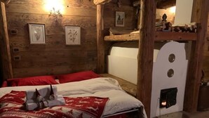 A wooden cabin-style room with a bed, red and white bedding, framed botanical prints, a fireplace, and a rustic wooden shelf.