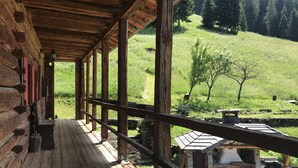 A wooden cabin with a porch overlooking a green hillside.