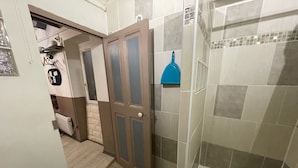 Une salle de bain avec une douche, des murs carrelés, un plancher en bois et une porte dotée de panneaux en verre dépoli.