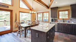 Una cocina amplia con una isla grande, armarios de madera oscura y ventanas grandes que ofrecen vistas al exterior.