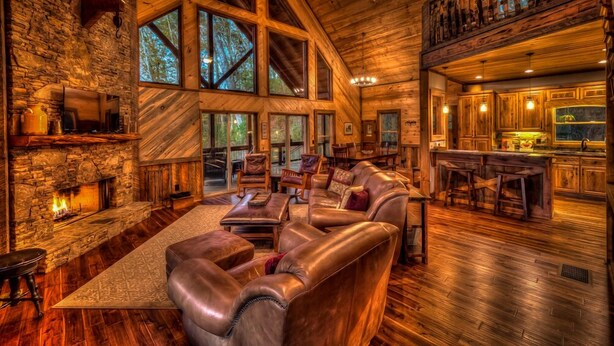 A spacious living room with leather sofas, a stone fireplace, and large windows offering a view of the outdoors.