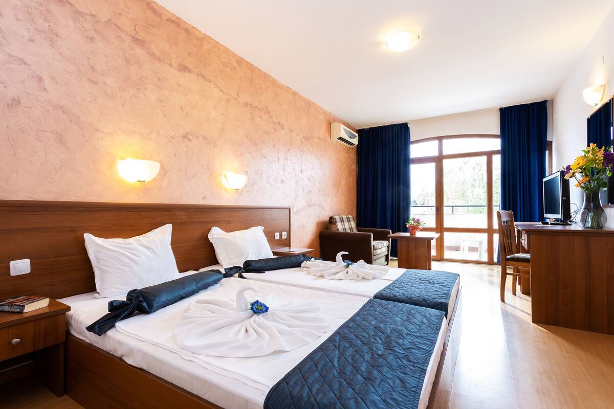 A hotel room with two beds, a desk, a chair, and a TV.