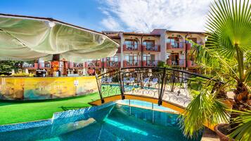 A pool area with a clear view of the pool, a pool bar, and a building with balconies in the background.