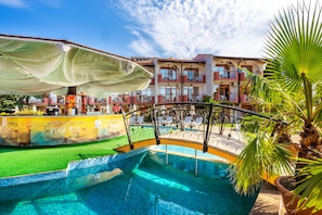 Zona de piscina con vista despejada, un bar junto a la piscina y un edificio con balcones al fondo.
