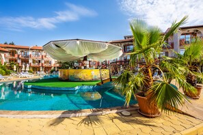A swimming pool with lounge chairs and a pool bar, surrounded by palm trees and a hotel building. - Complex Sunrise All Inclusive (Sunny Beach)