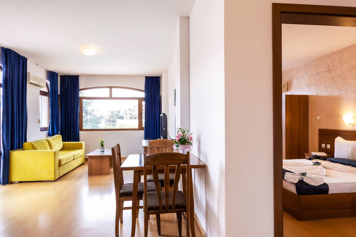 A hotel room with a bed, a yellow sofa, a wooden dining table, and a chair.