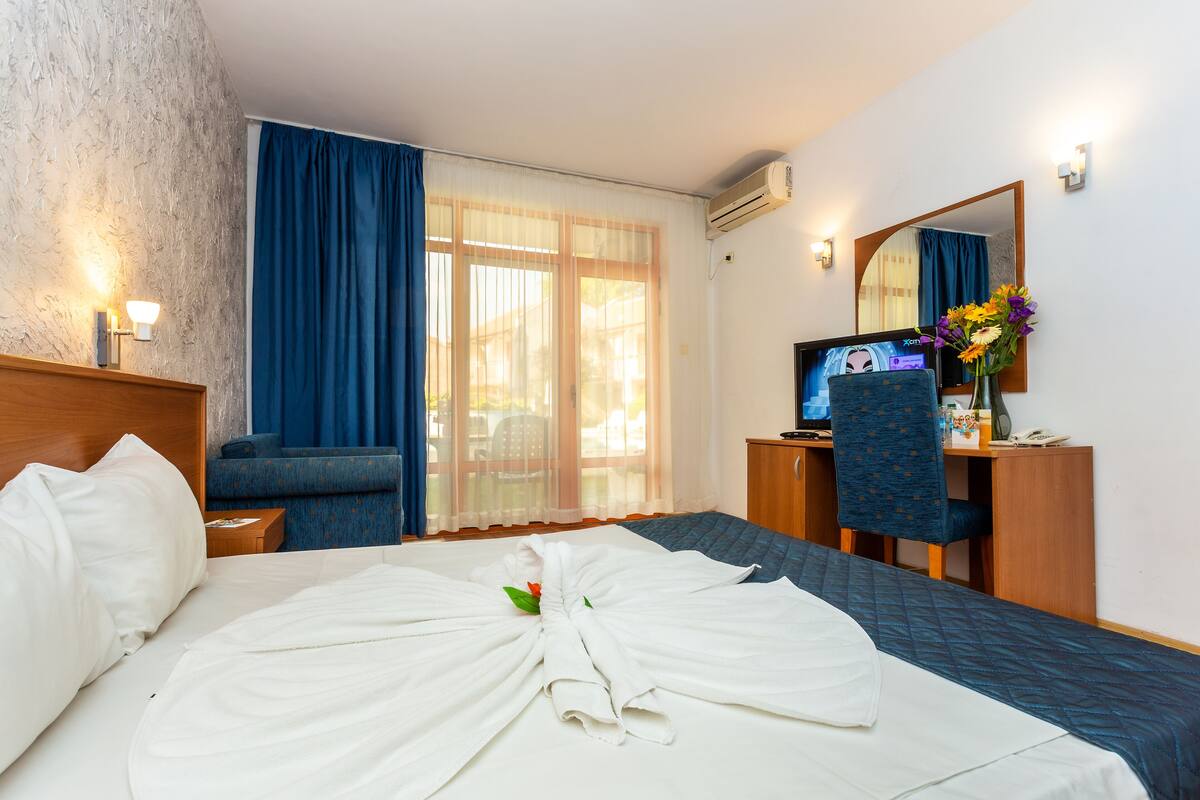 A hotel room with a bed, a desk, a chair, a television, and a mirror.