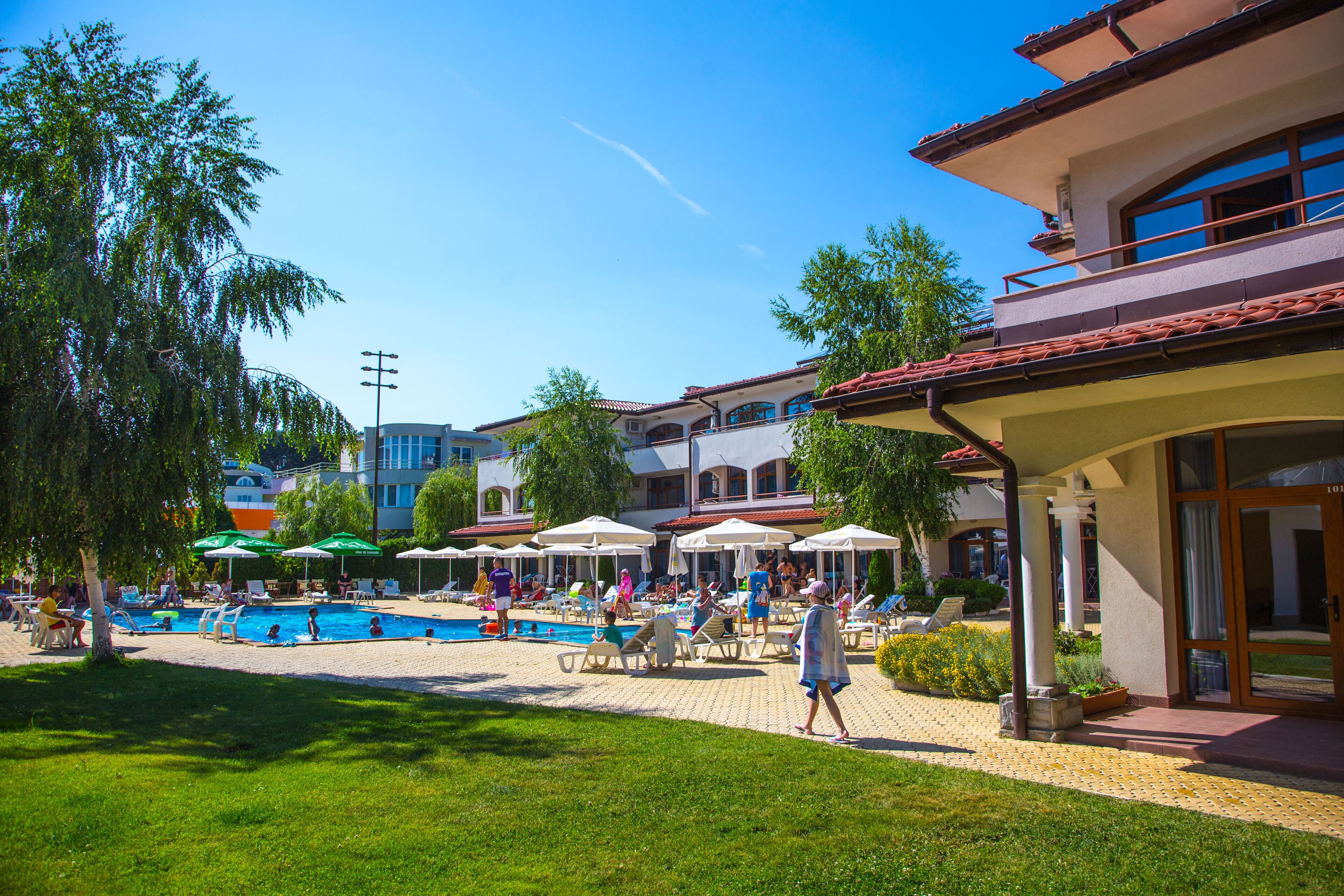 A pool area with lounge chairs and umbrellas, surrounded by buildings with balconies and a clear sky.