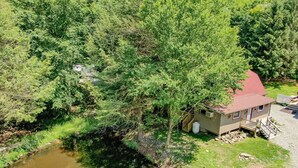 A small cabin with a red roof, surrounded by dense greenery and a pond. - Roscoe Cottage Pet Friendly  (Roscoe)