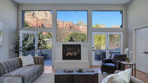 Un salón amplio con chimenea, ventanas grandes que ofrecen vistas a formaciones rocosas rojizas y una zona de estar acogedora.
