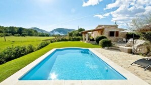 A rectangular swimming pool with a stone border, surrounded by a well-maintained lawn and a stone patio with outdoor furniture. - QUIET FINCA CAN XAVI (Alcudia)