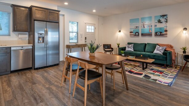 A modern kitchen with a stainless steel refrigerator, wooden dining table, and chairs. There is a green sofa and a colorful rug in the living area. - Close to it all!  Long Beach 5bed/4bath (Long Beach)