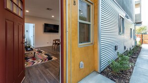 A modern house with a wooden front door, a visible room with a television, and a small outdoor area with a plant. - Close to it all!  Long Beach 5bed/4bath (Long Beach)