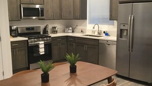 A modern kitchen with dark wooden cabinets, stainless steel appliances, a wooden dining table with two chairs, and a potted plant on the table. - Close to it all!  Long Beach 5bed/4bath (Long Beach)