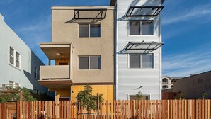 A multi-story residential building with balconies, a wooden fence, and a clear blue sky. - Close to it all!  Long Beach 5bed/4bath (Long Beach)