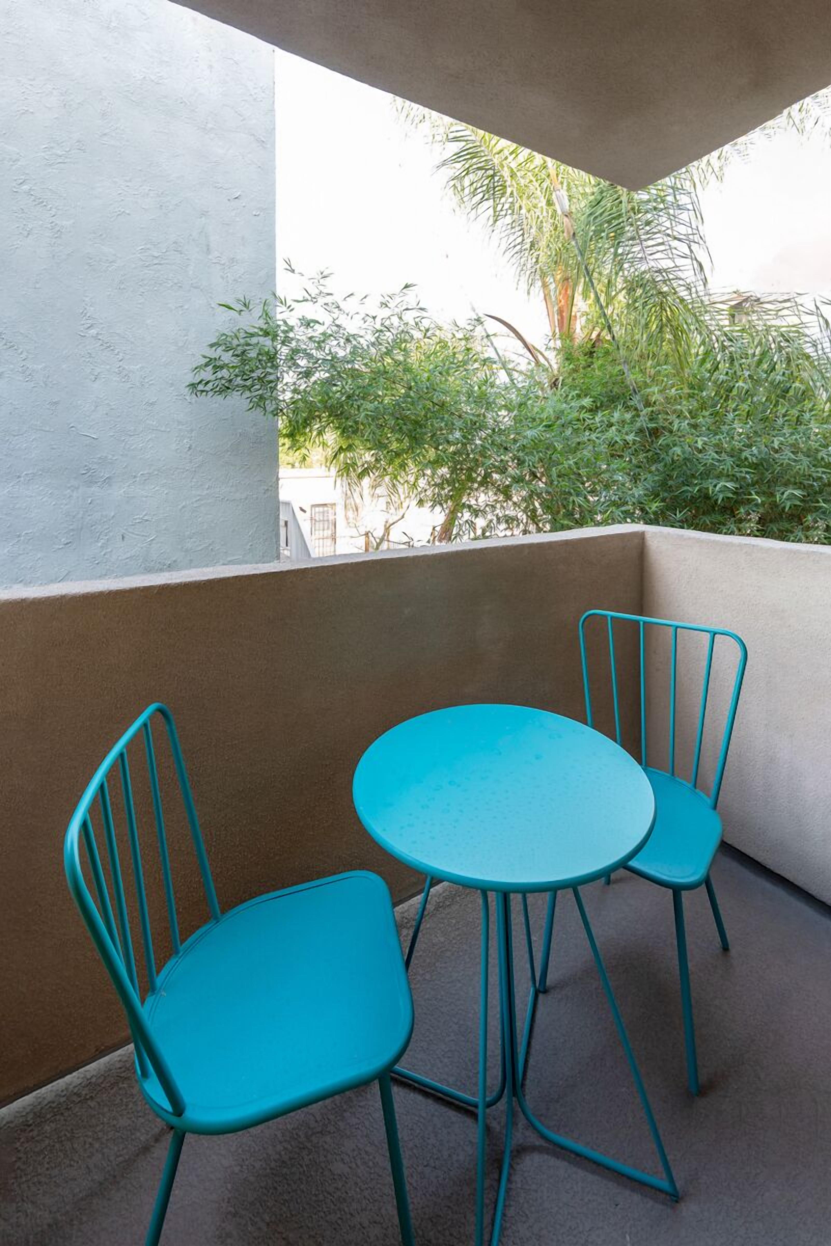 A small balcony with two turquoise metal chairs and a round table.