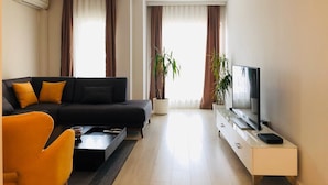 A modern living room with a black sofa, a yellow armchair, a flat-screen TV, and two potted plants. - Downtown Apartments (Pristina)