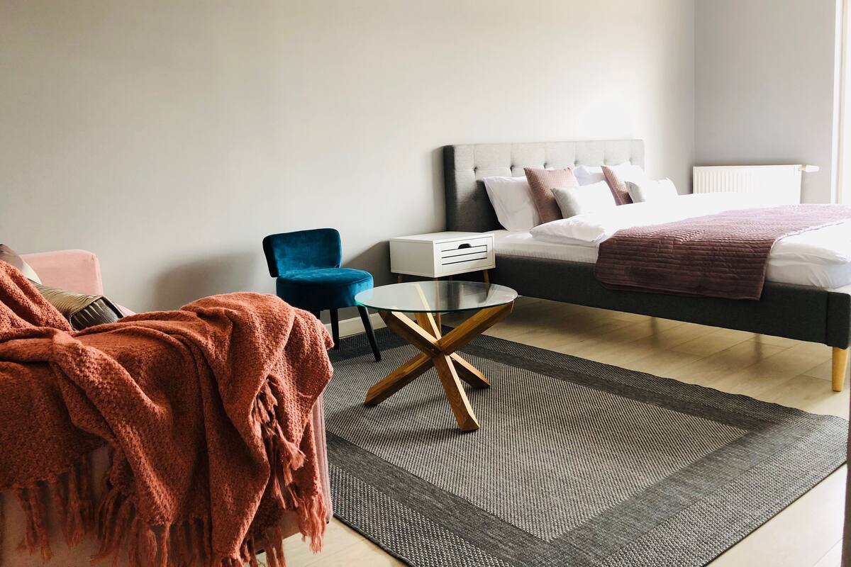 A modern bedroom with a bed, a chair, a small table, and a blanket.
