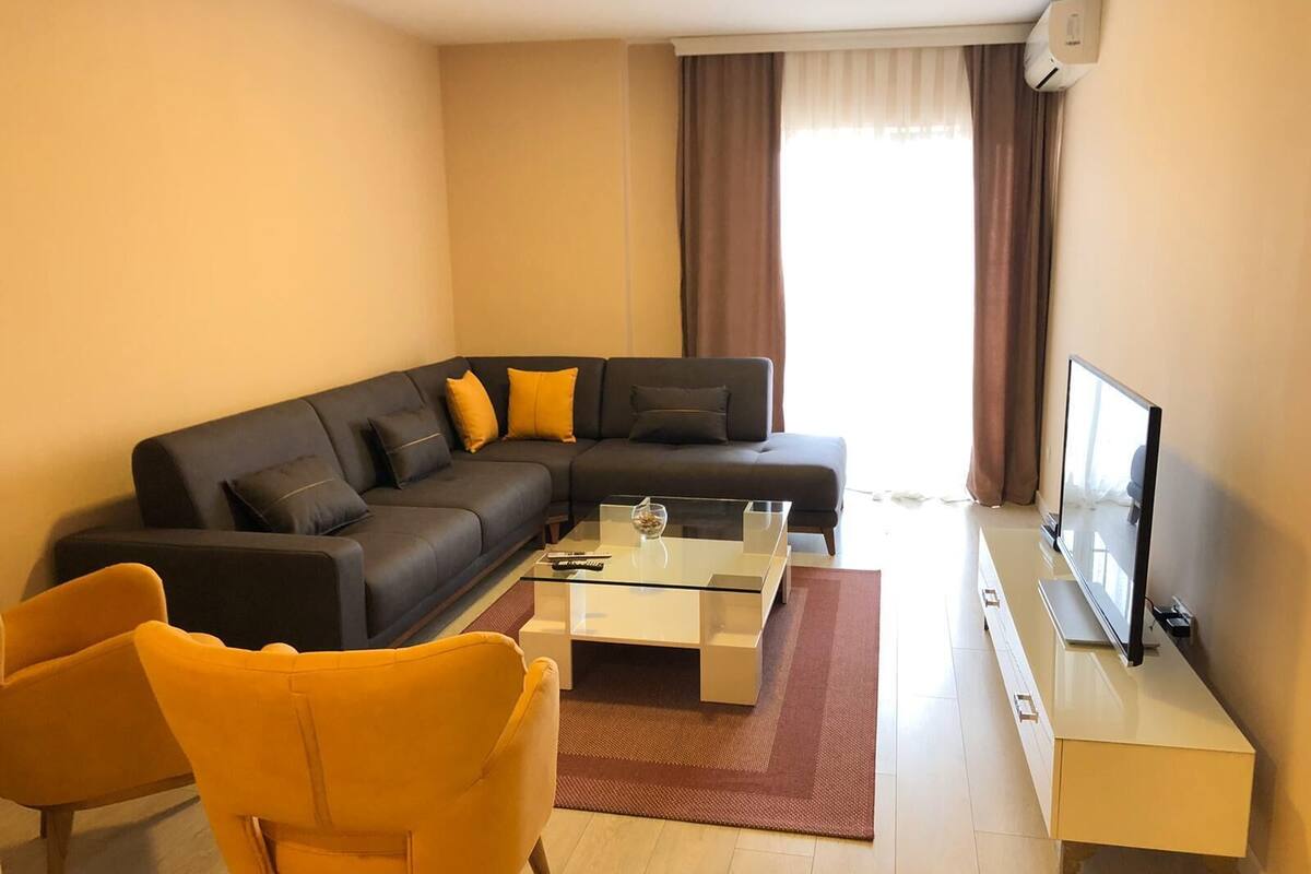 A modern living room with a sectional sofa, a glass coffee table, and a flat-screen TV.