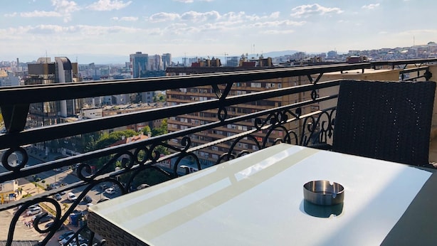 A balcony with a metal railing, a table, and a metal bowl. - Downtown Apartments (Pristina)