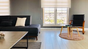 A modern living room with a dark grey sofa, a glass coffee table, and a black armchair. - Downtown Apartments (Pristina)