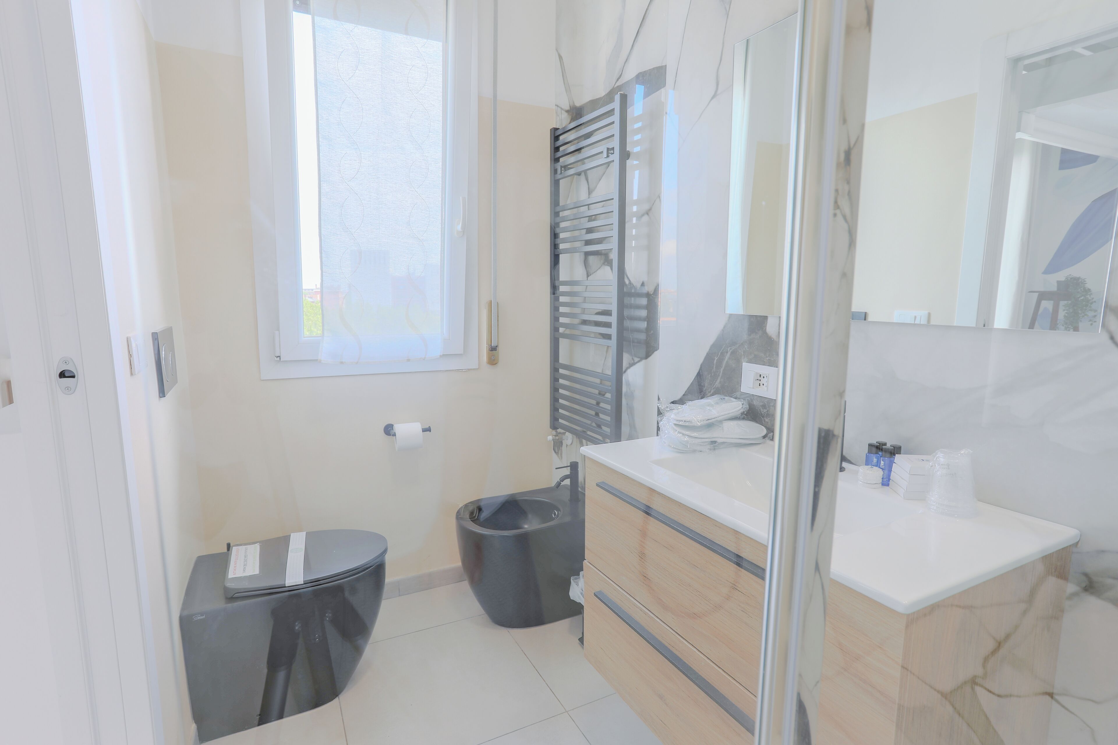 A modern bathroom with a toilet, bidet, vanity with a mirror, and a window.