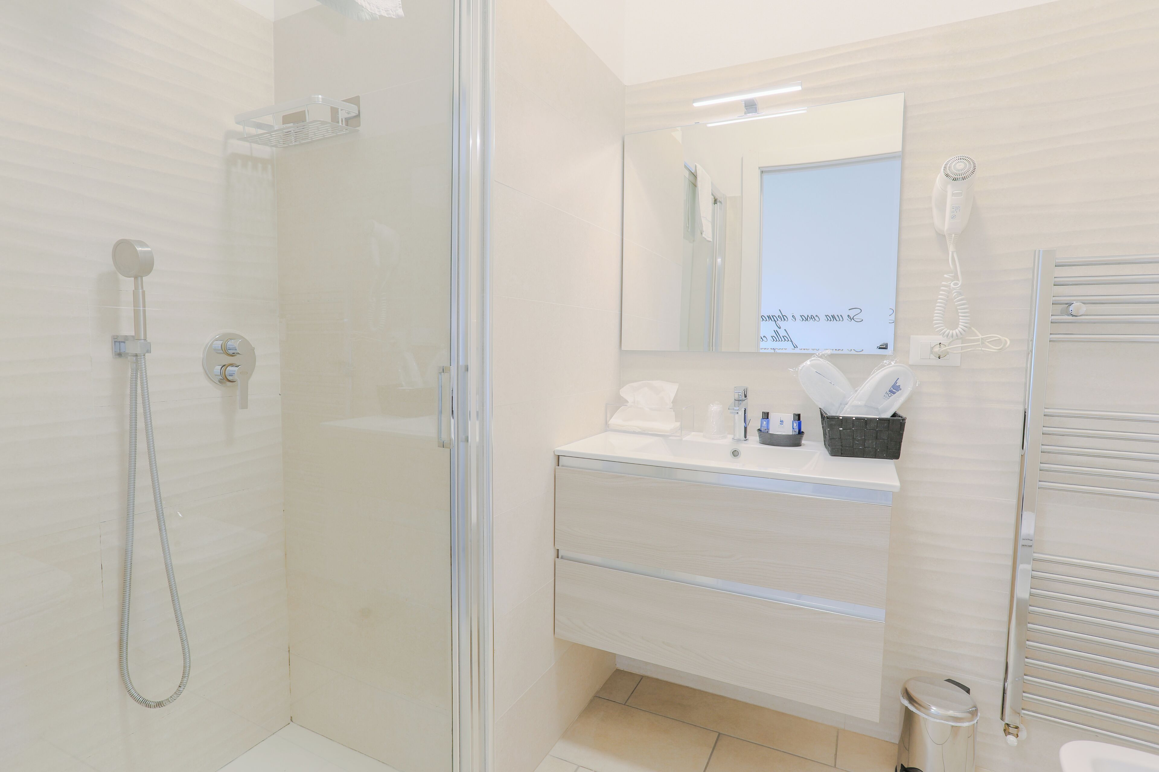 Un baño moderno con ducha envuelta en vidrio, un tocador blanco con espejo y un perchero.